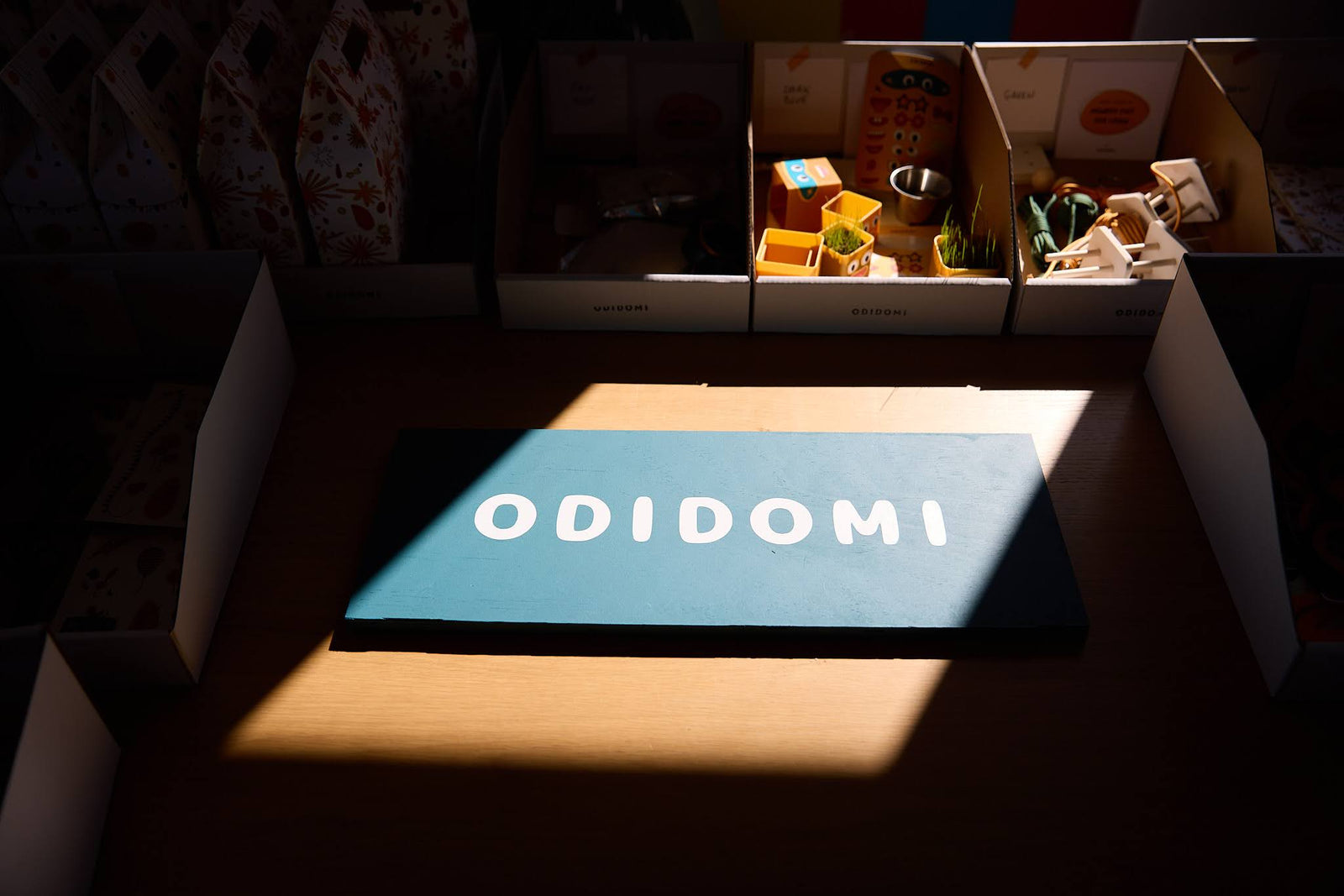 ODIDOMI teal sign illuminated by sunlight, surrounded by open kit boxes and party favor components
