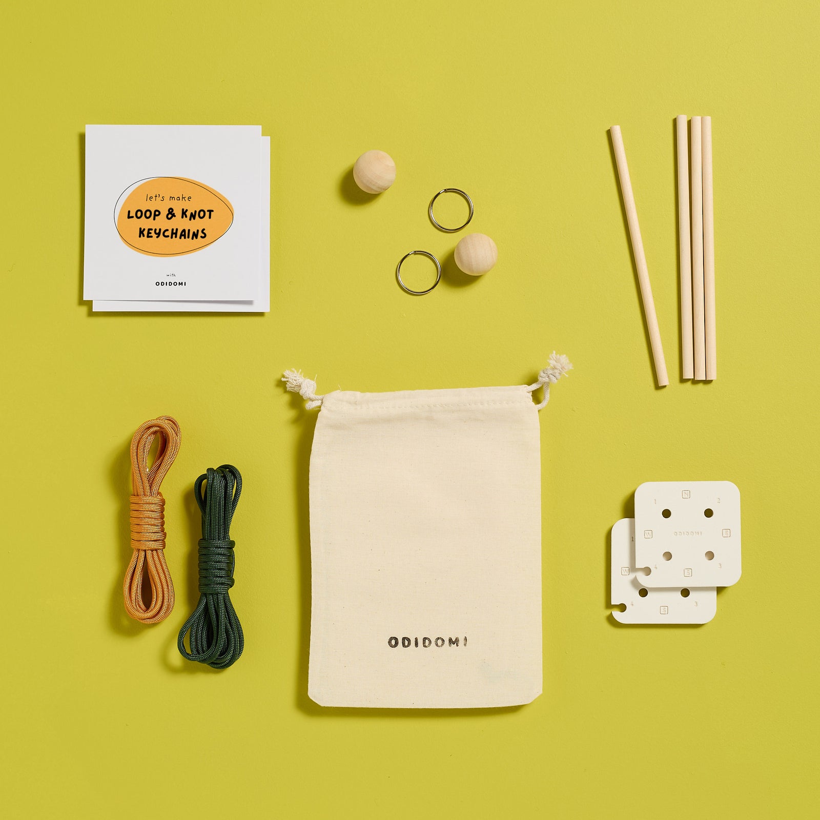 Flat lay of ODIDOMI’s Loop & Knot Keychain Kit on a yellow background. This DIY craft kit includes paracord, wooden beads, keyrings, dowels, a cotton drawstring bag, and instructions—designed in-house by ODIDOMI, a family-run brand creating high-quality, handcrafted goodie bags and party favors for kids.
